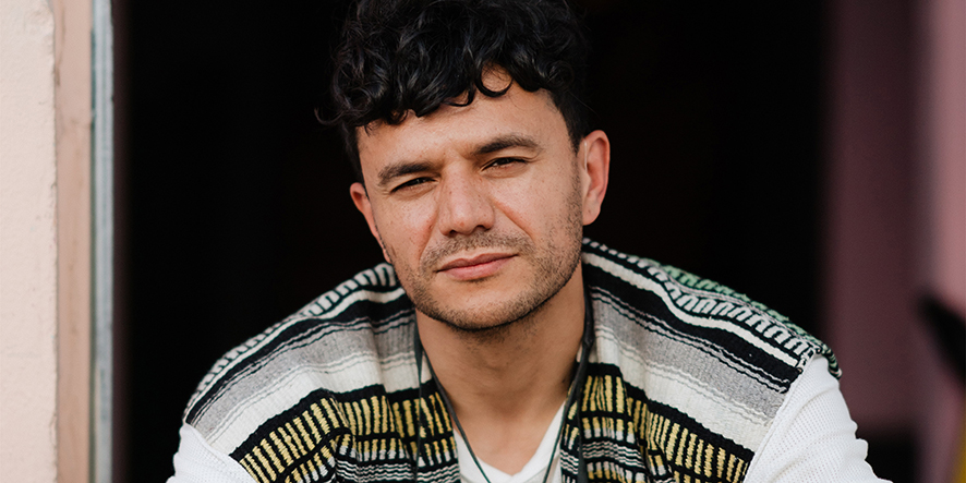 A portrait photo of Raymond Antrobus, looking directly into the camera. He is wearing a striped top.